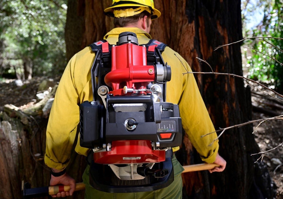 la pompe portable MARK-3@ de WATERAX Un homme vêtu d'une veste jaune porte une pompe rouge attachée dans le dos.